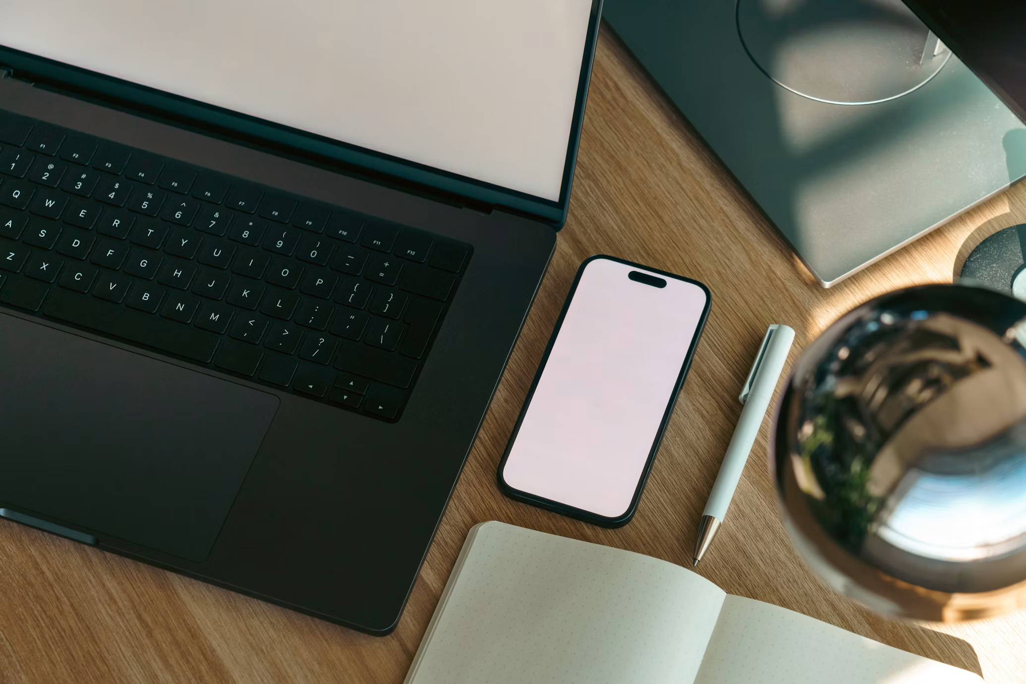 A laptop, phone, and notebook on a desk, mid-work